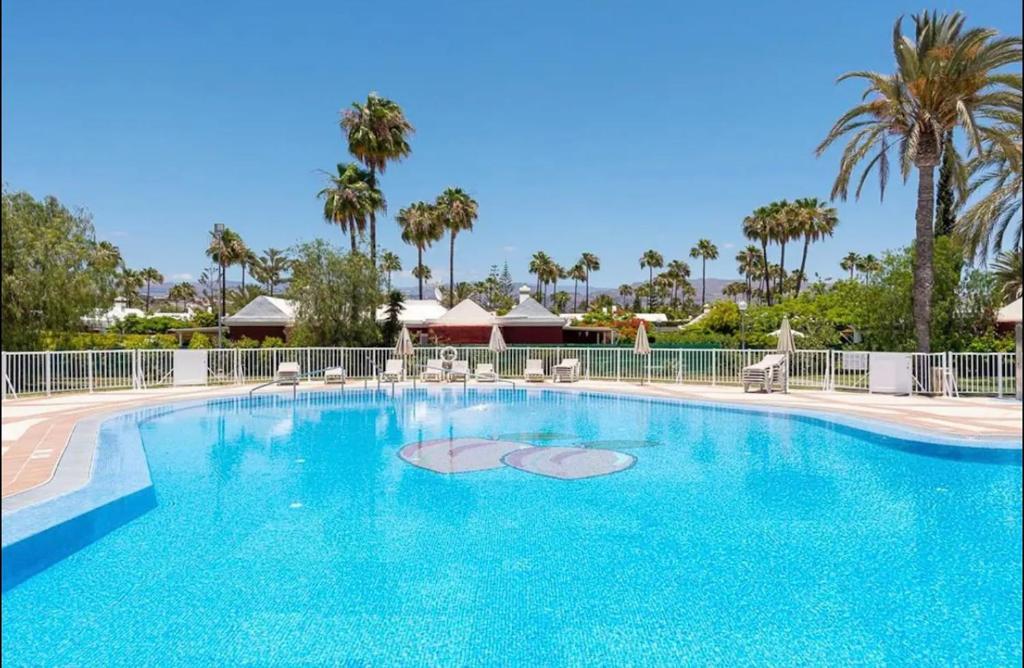 a large blue pool with chairs and palm trees at Espacioso Bungalow en Maspalomas in Maspalomas