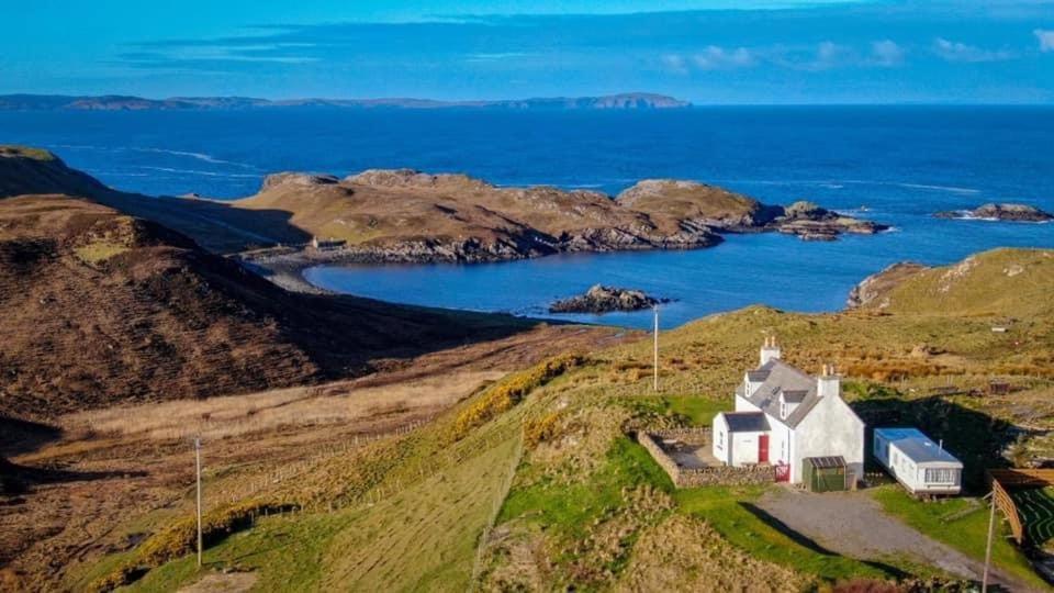 an island with a white house on a hill next to the ocean at Cnoc Ard in Scourie