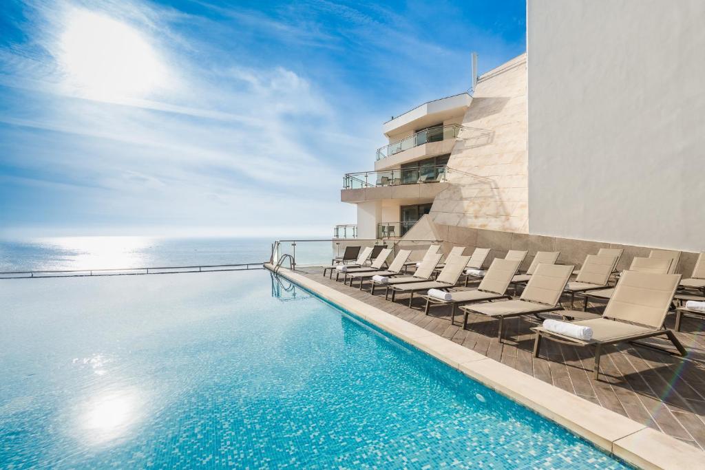 einen Pool mit Stühlen und das Meer im Hintergrund in der Unterkunft Sesimbra Oceanfront Hotel in Sesimbra