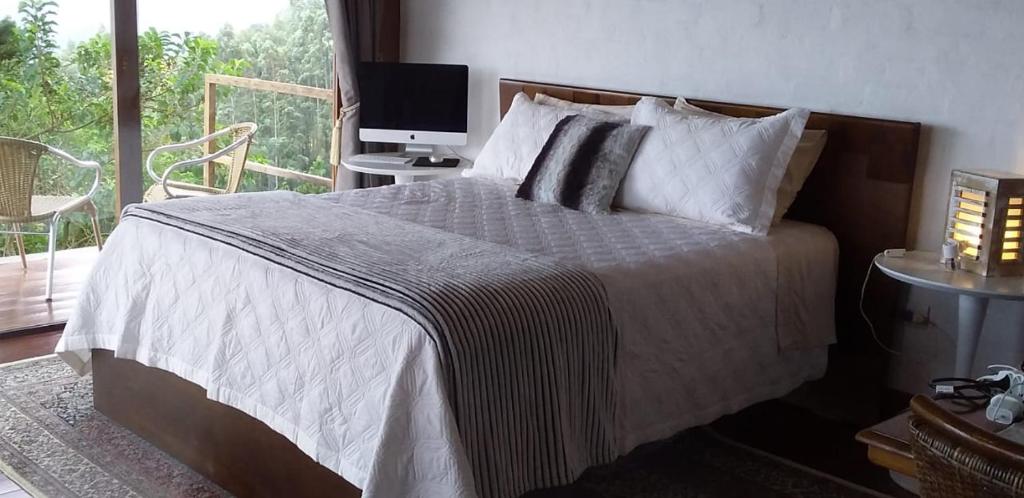 um quarto com uma cama, uma televisão e uma janela em Clorofila Hospedaria em São Bento do Sapucaí