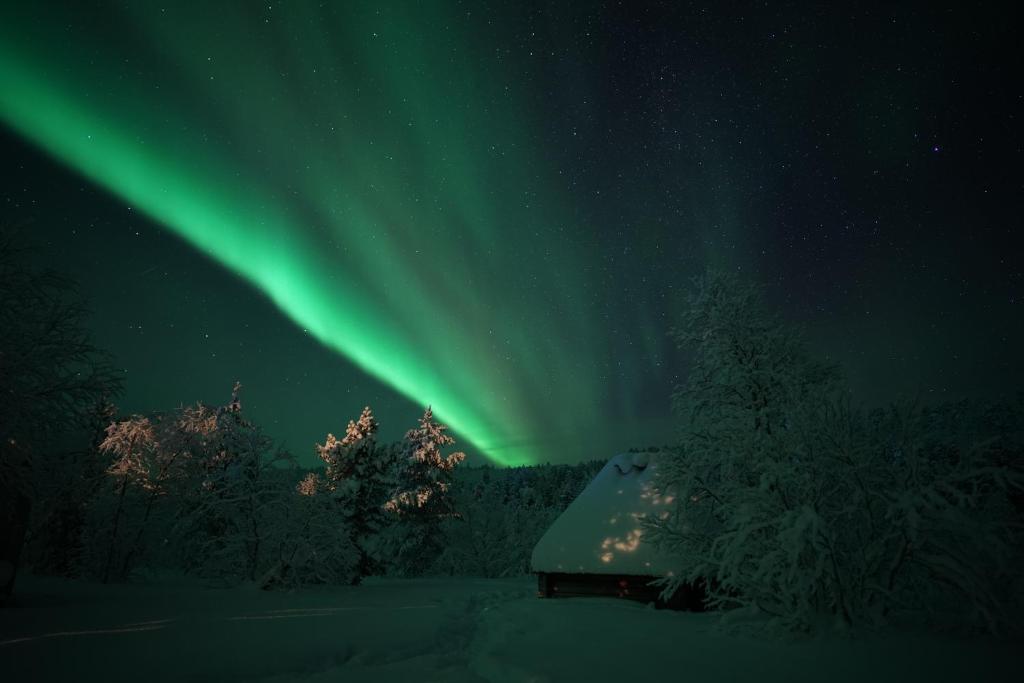 une aurore brille dans le ciel au-dessus d'une cabine dans l'établissement Muotkan Ruoktu Tunturikyla, à Inari