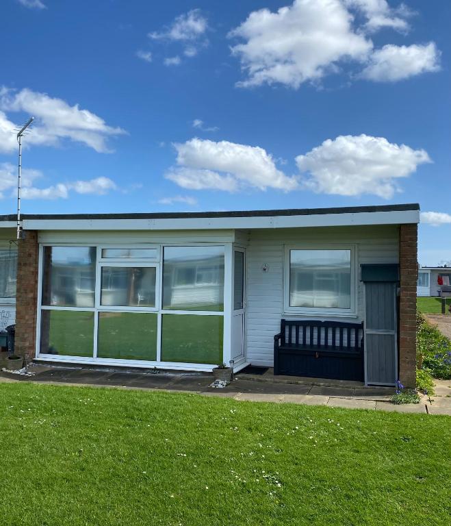a small house with a porch and a green lawn at 95 Sundowner, Hemsby, Norfolk in Hemsby