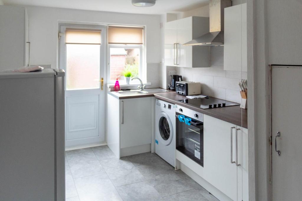 cocina con armarios blancos, lavadora y secadora en Linwood House en Paisley