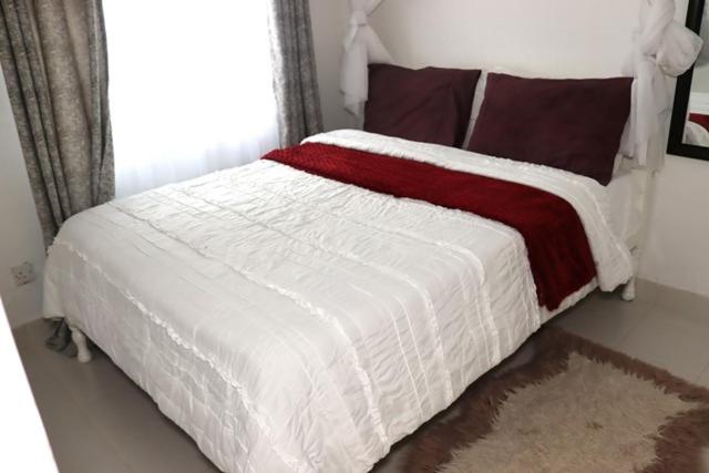 a white bed with a red and white blanket on it at Aisura place in Nairobi