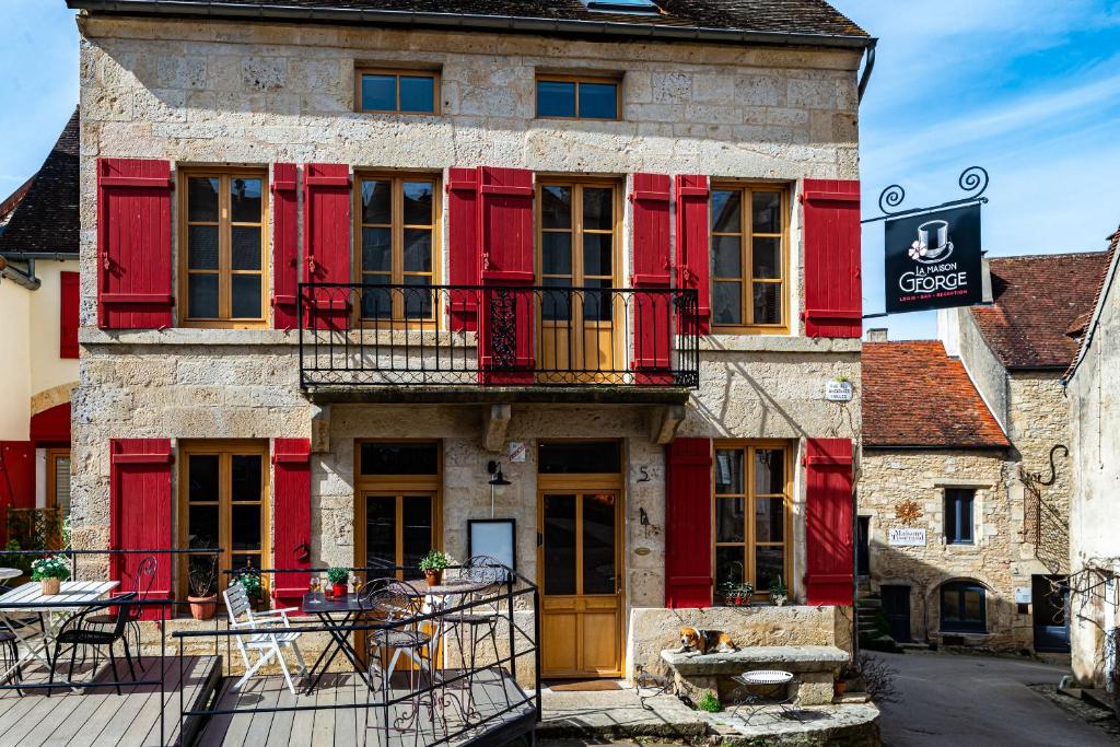 un vecchio edificio con finestre con persiane rosse e un tavolo di La Maison George a Flavigny-sur-Ozerain