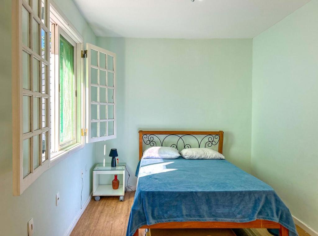 a bedroom with a bed with a blue blanket and two windows at Otima casa com lazer completo em Sao Conrado RJ in Rio de Janeiro