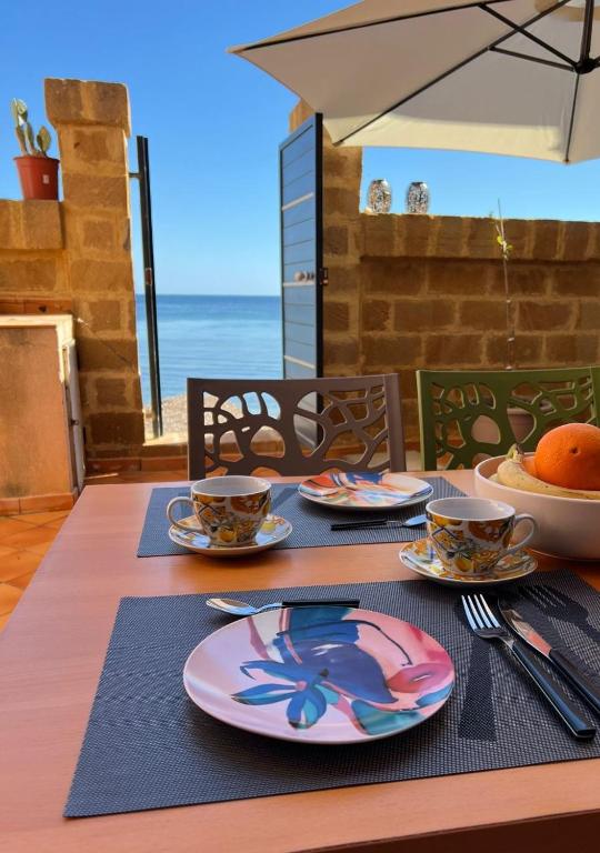 a table with plates and cups on a table with the ocean at Gioia di Mare in Marzamemi