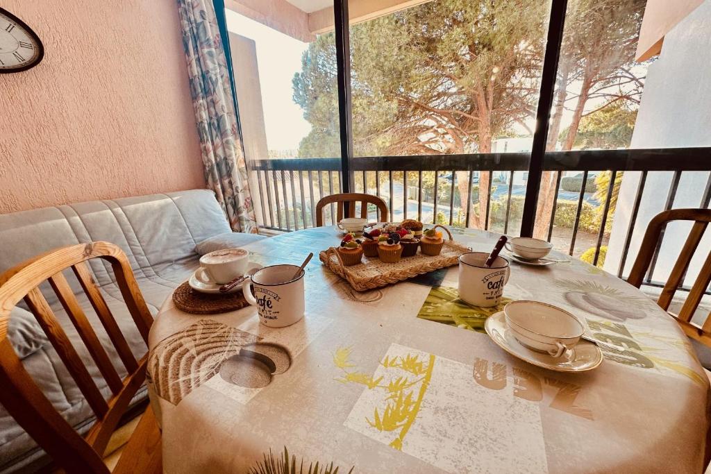 une table avec des assiettes et des tasses et une fenêtre dans l'établissement Triangle de la Baronnie Appartement 1 chambre proche de la Mer, au Grau-du-Roi