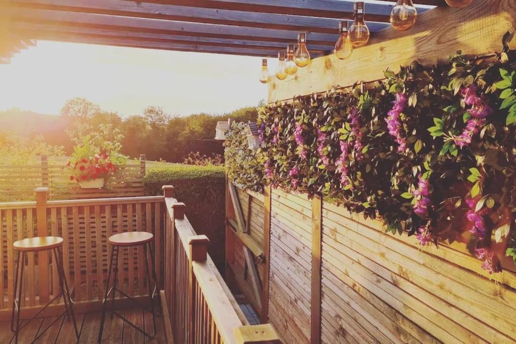 een patio met 2 krukken en bloemen op een hek bij Sunset View in Gillingham