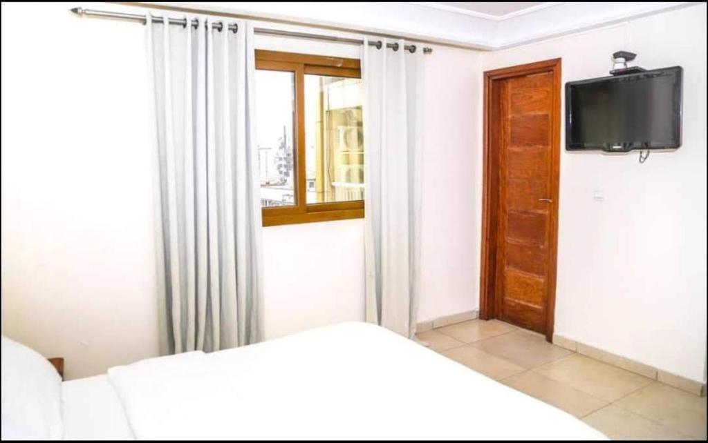 a bedroom with a bed and a tv and a window at Hannatel Rooms Liberté in Douala