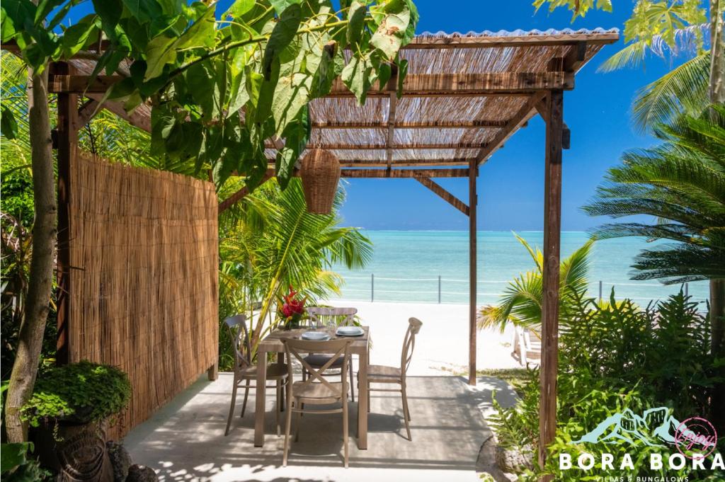 uma mesa e cadeiras debaixo de uma pérgula na praia em Matira Sunset House N659 DTO-MT em Bora Bora