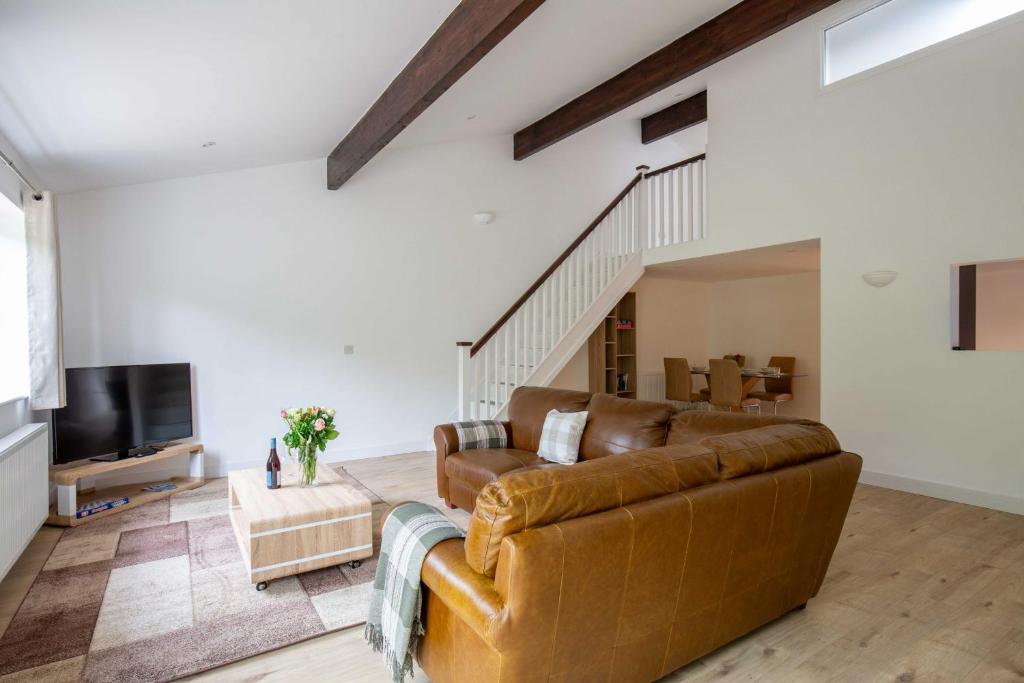 ein Wohnzimmer mit einem braunen Ledersofa und einem TV in der Unterkunft Ascot Cottage in Cirencester