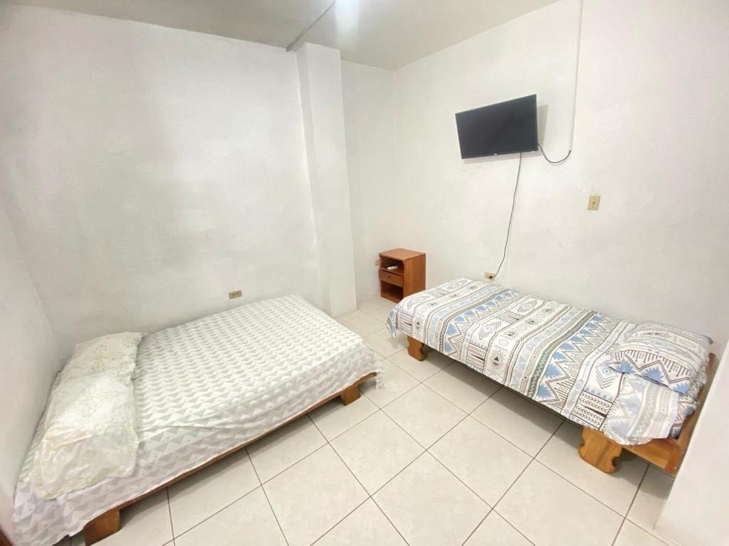 a bedroom with two beds and a tv on the wall at Ballesteros Apartaments in Puerto Ayora