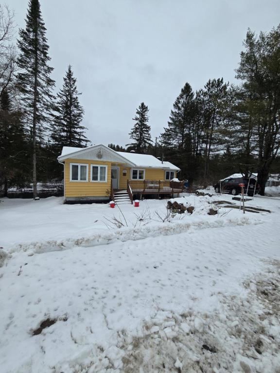 une maison jaune dans une cour avec de la neige au sol dans l'établissement CITQ 303469.CHALET OASIS DE PAIX. BORD DE L’EAU.4 SAISONS.À LOUER, à Chertsey