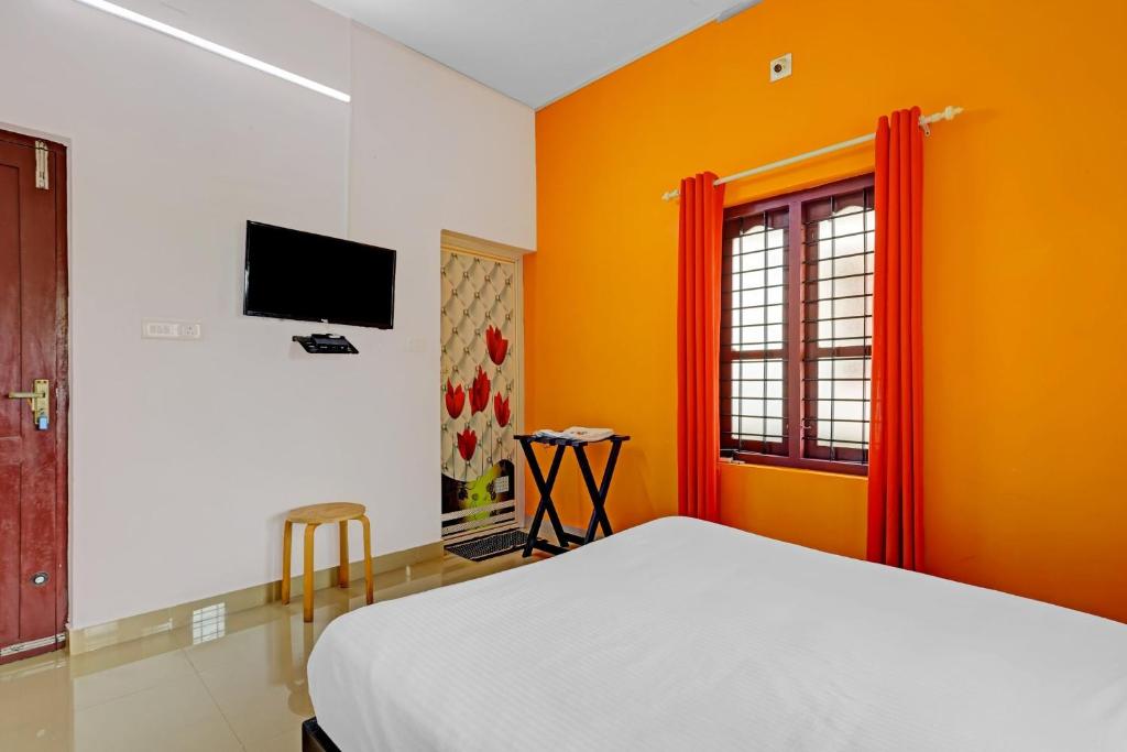 a bedroom with orange walls and a bed and a television at Capital O 84184 Pop Tavern Kazhakkottam in Vettutura