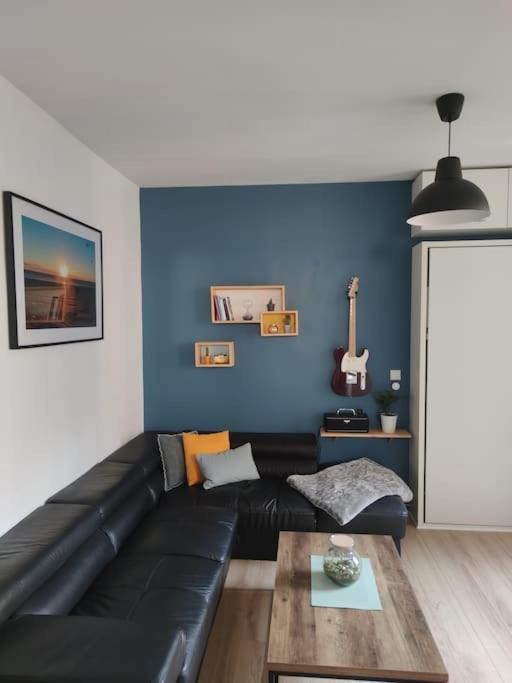 un salon avec un canapé en cuir noir et un mur bleu dans l'établissement Le nid douillet - Cosy and very close to Paris, à Asnières-sur-Seine