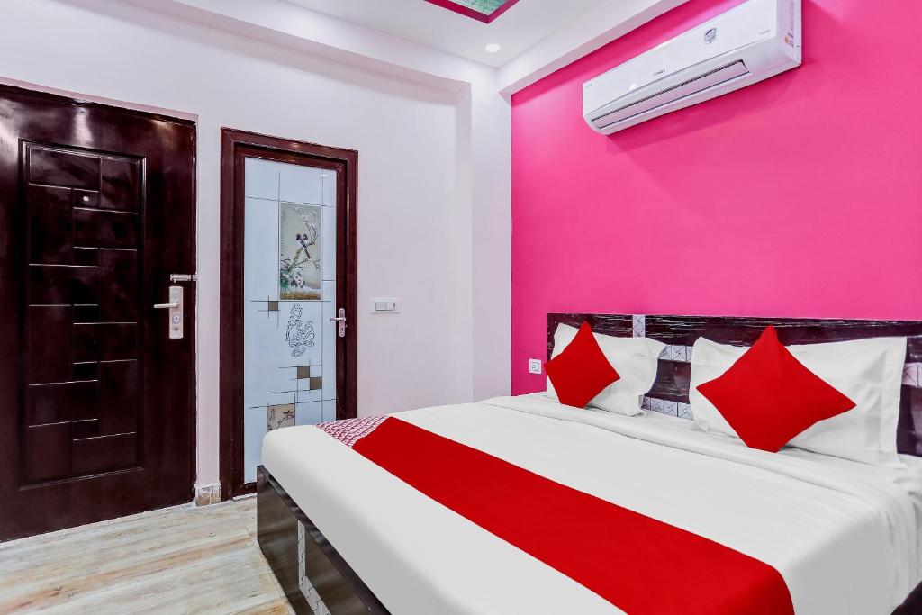 Un dormitorio con una pared rosa y una cama con almohadas rojas. en Super OYO The Prima Residency, en Ghaziabad