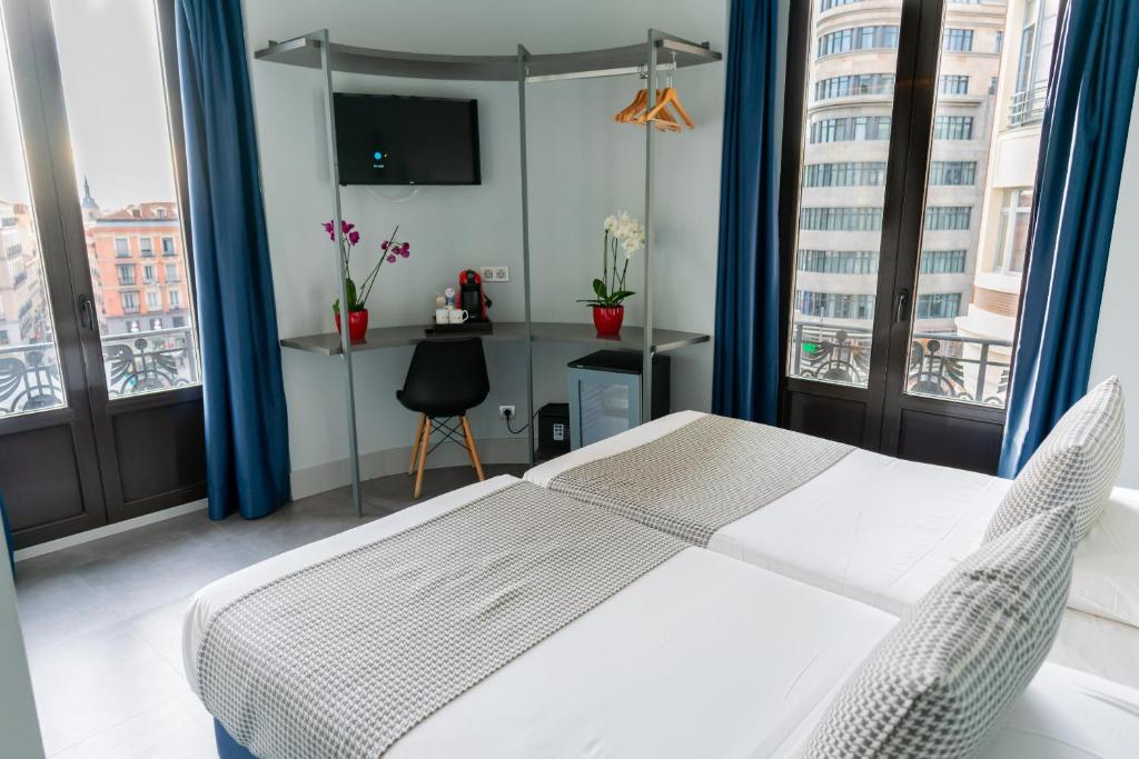 a bedroom with a white bed and two large windows at Hostal Carmen-Gran Vía in Madrid
