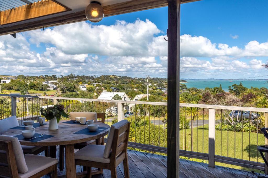 a dining table on a deck with a view of the ocean at Surfdale Sunspot Spa Escape Waiheke in Oneroa