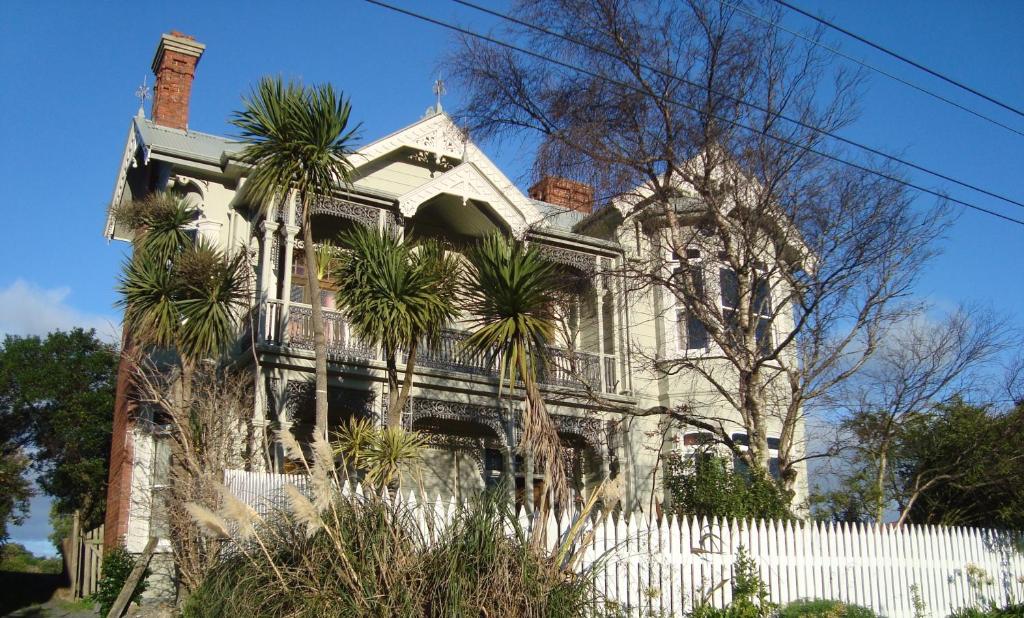 an old house with a white fence and palm trees at Artica Art & Accommodation in Dunedin