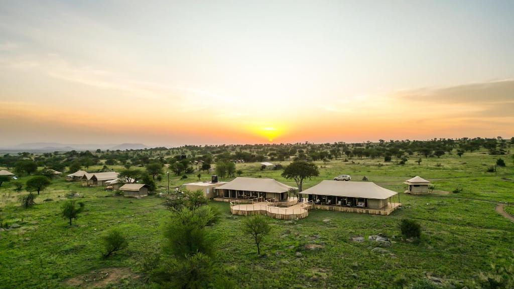 a group of lodges in a field with the sunset at Serengeti Malaika Luxury Camp in Serengeti National Park