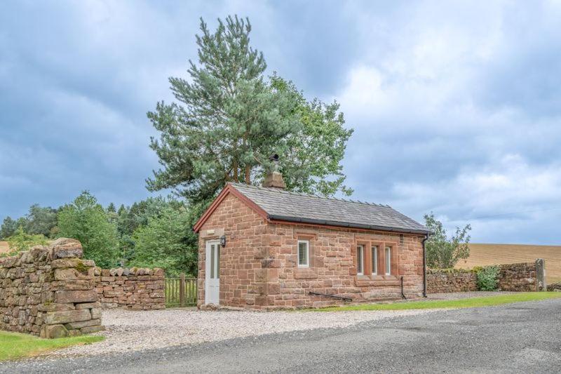 um pequeno edifício de tijolos com uma parede de pedra em The Railway Weigh Office (Cliburn) em Penrith