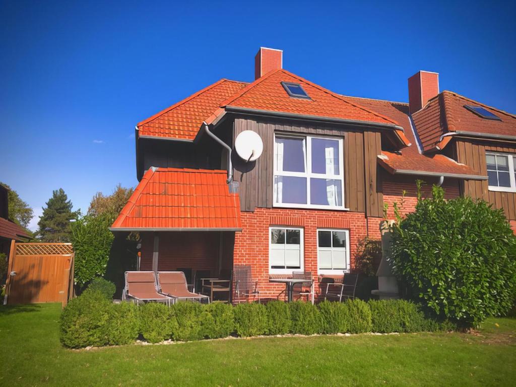 une maison avec un toit orange et des chaises dans la cour dans l'établissement F4a EG - Fasanenblick, à Petersdorf auf Fehmarn