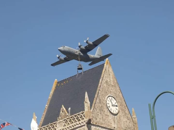 a plane flying over a building with a clock on it at Gite de la longue fosse in Mandeville-en-Bessin