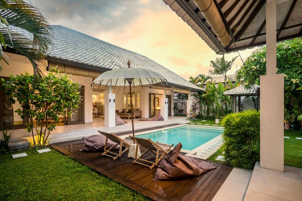 a villa with a swimming pool and two chairs and an umbrella at Villa Moju Canggu by Alfred in Bali in Canggu