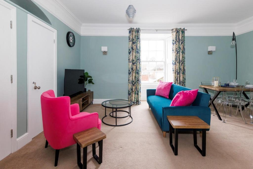 a living room with blue and pink chairs and a table at St Richard's Apartment in Chichester