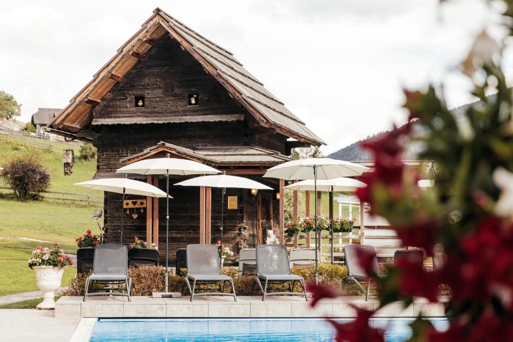 a building with chairs and umbrellas next to a pool at Thermenwelt Hotel Pulverer in Bad Kleinkirchheim
