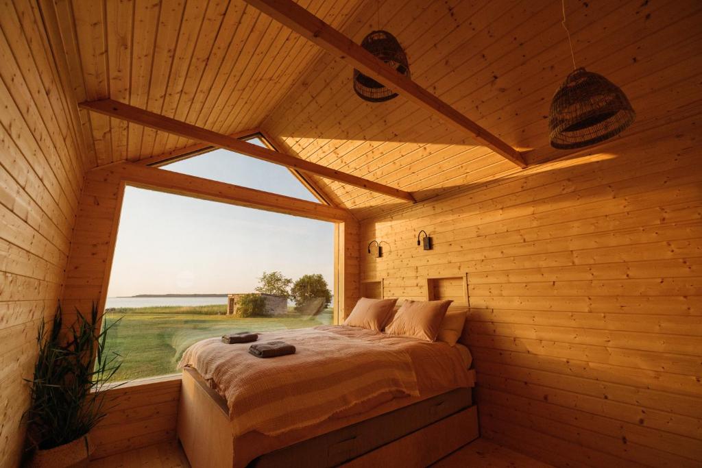 ein Schlafzimmer mit einem Bett in einem Holzzimmer mit einem Fenster in der Unterkunft Sunset Bungalow in Orissaare