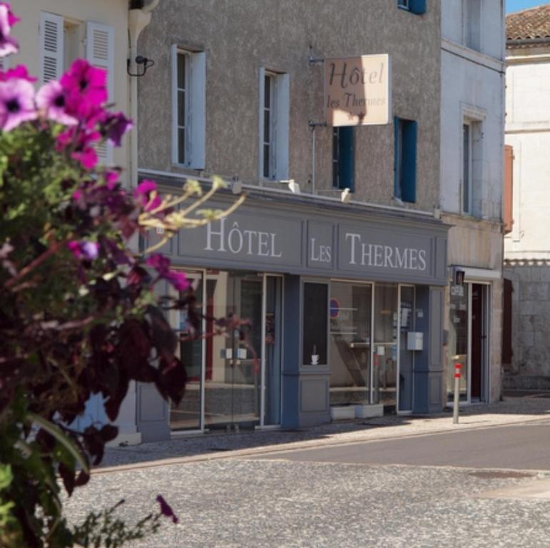 a store on a street with pink flowers in the foreground at Hôtel Les Thermes in Jonzac