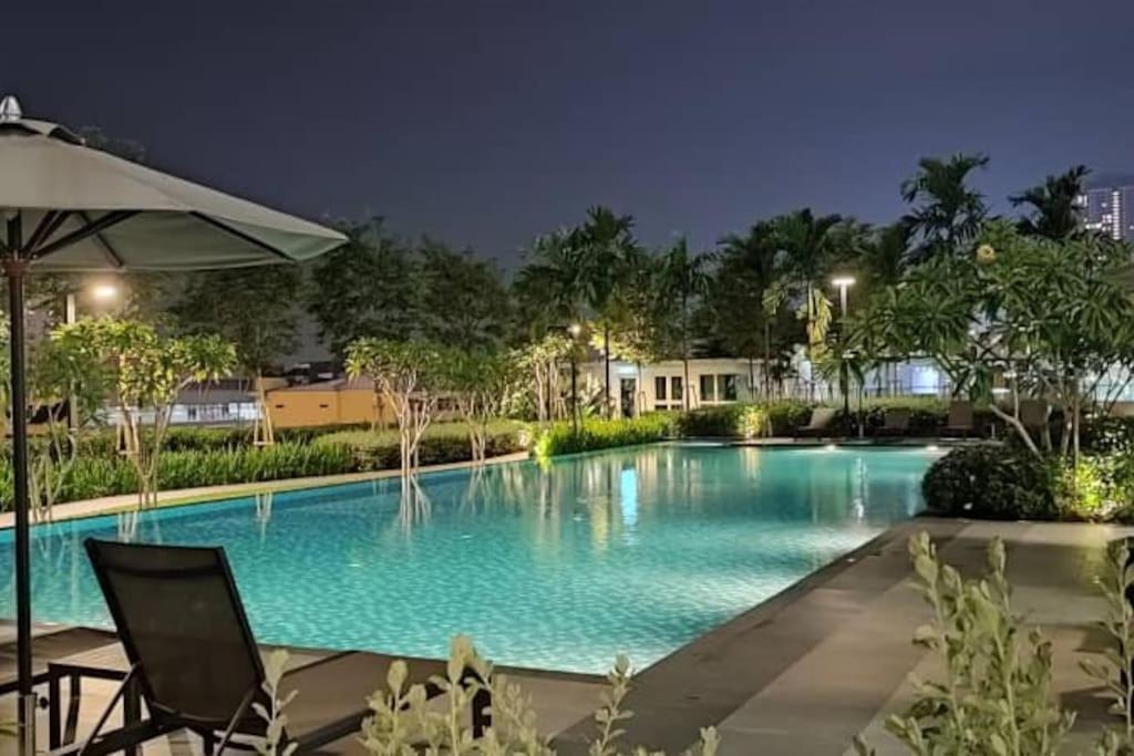 uma piscina à noite com duas cadeiras e um guarda-sol em Affordable Residence Plaza @ KJ em Petaling Jaya
