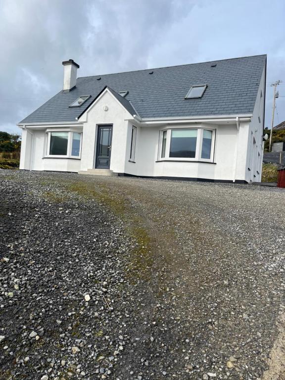 a white house with a roof on a gravel driveway at Beach View Heights Dugort Achill Eircode F28E8D9 in Doogort