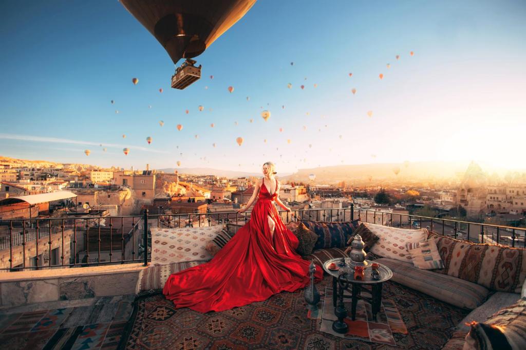 uma mulher num vestido vermelho de pé numa varanda com balões em Zara Cave Hotel em Goreme