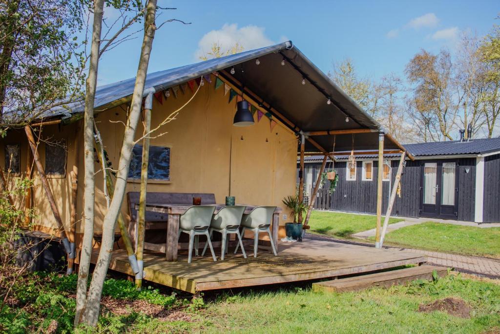 ein Haus mit einem Tisch und Stühlen auf einer Terrasse in der Unterkunft Glamping-tent 'Yatra Nirvana' met privé keuken en regendouche in Grou