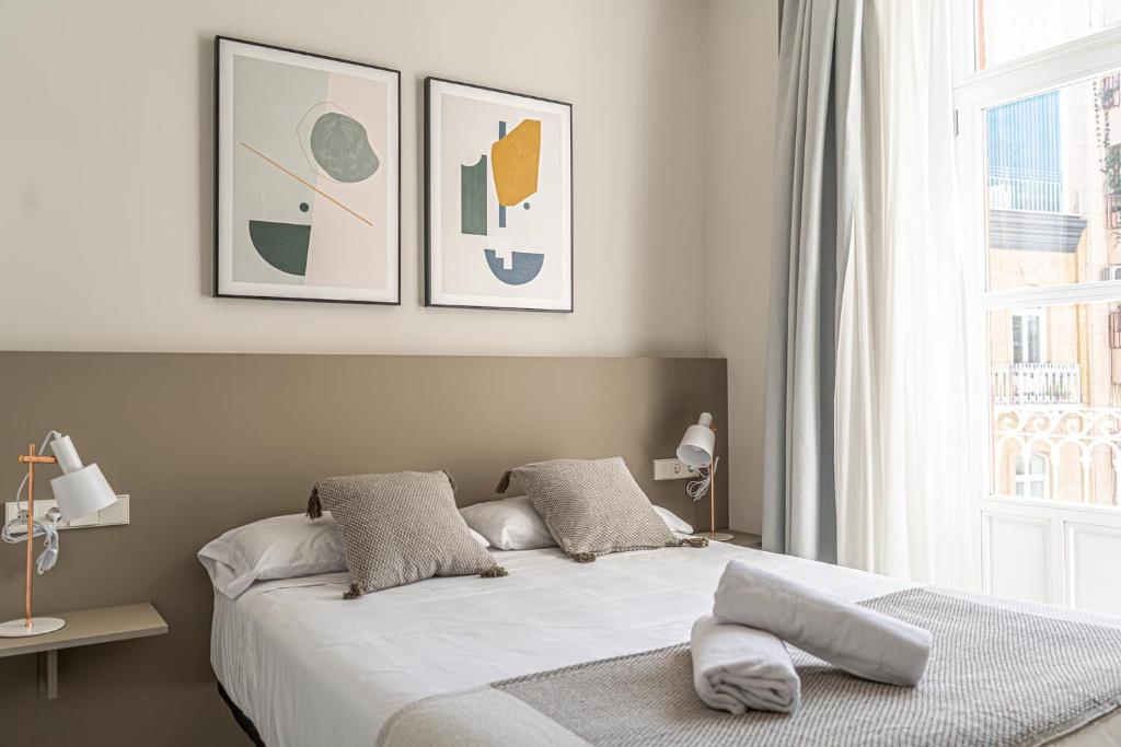 ein Schlafzimmer mit einem Bett mit zwei Kissen und einem Fenster in der Unterkunft Apartamentos Turísticos Plaza del Rey in Cartagena