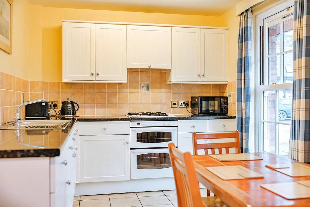 cocina con armarios blancos y mesa de madera en Finest Retreats - Netley Hall - Jasmine, en Dorrington