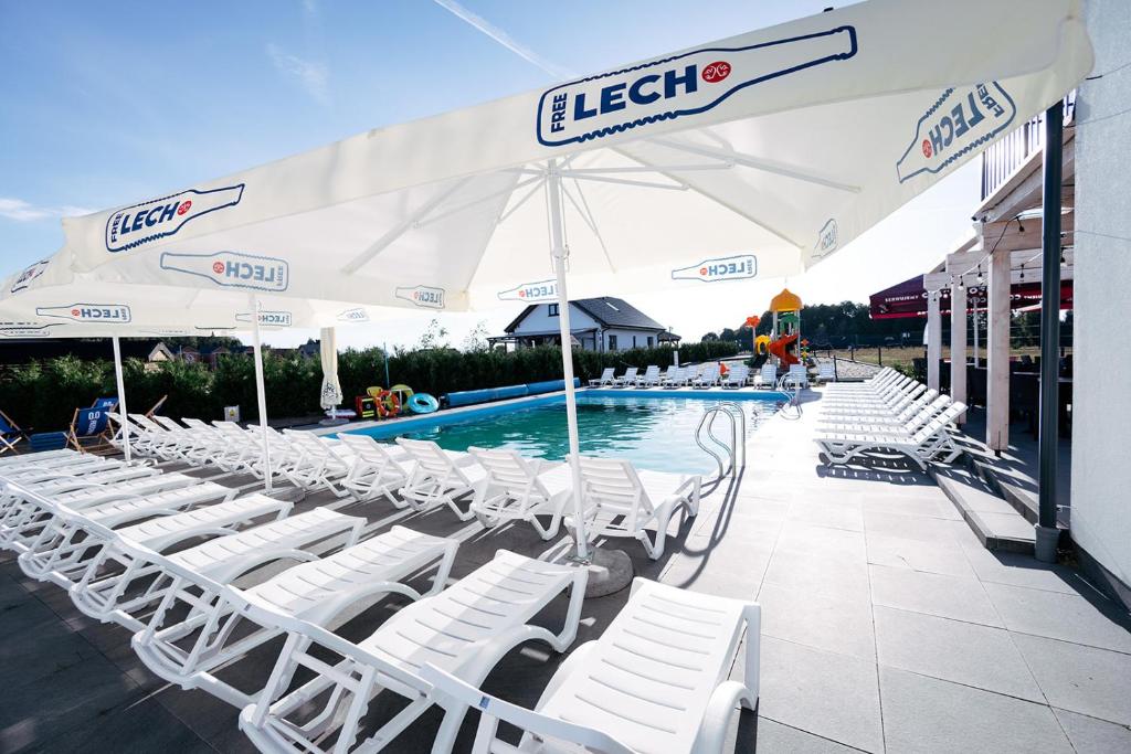a swimming pool with white chairs and an umbrella at Skorzęcin Rybakówka Resort in Skorzęcin