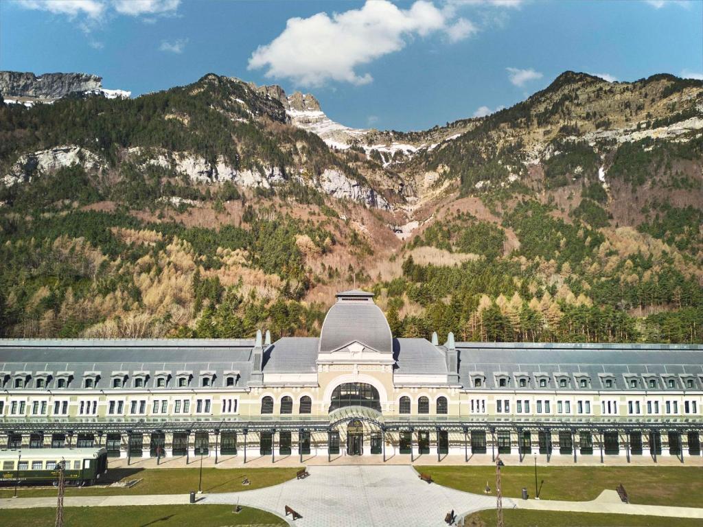 un gran edificio blanco con montañas en el fondo en Canfranc Estación, a Royal Hideaway Hotel - Gran Lujo, en Canfranc-Estación