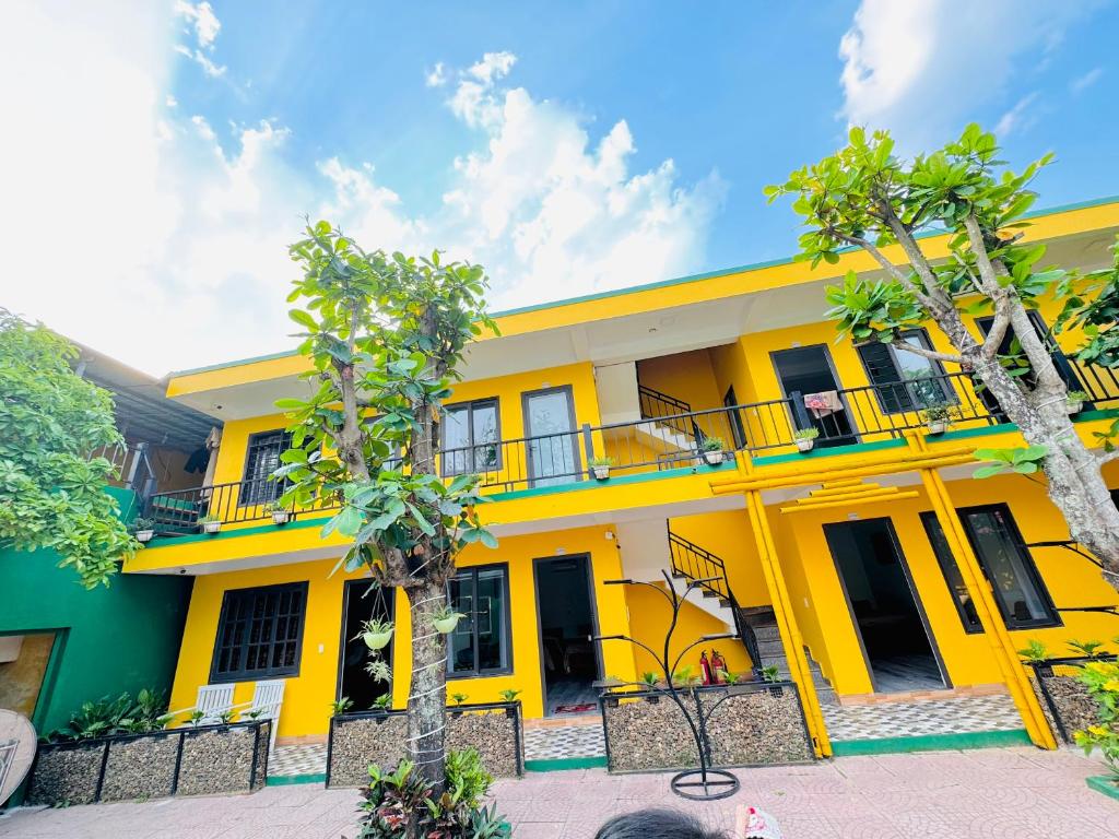 a yellow building with a balcony and two trees at Luti Homestay and Restaurant in Dong Hoi