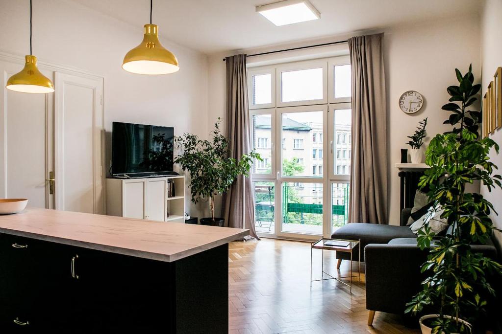 a living room with a kitchen and a living room with plants at Kraków Apartments - Balcony, Workspace, Tram stop - by Rentujemy in Krakow
