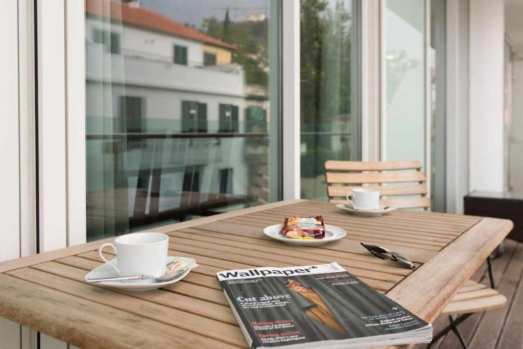 a wooden table with a magazine and coffee cups on it at Dolce Vita - City Center & Shopping Center in Funchal