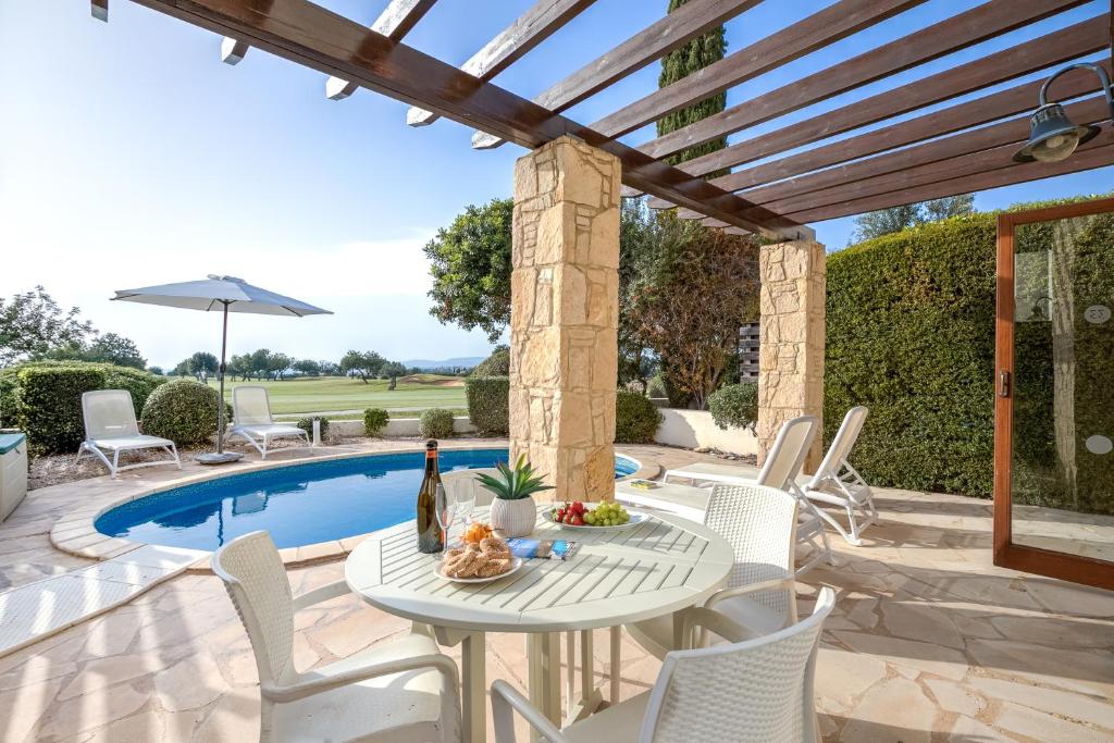 un patio con mesa y sillas junto a una piscina en 2 bedroom Villa Kornos with private pool and golf views, Aphrodite Hills Resort en Kouklia