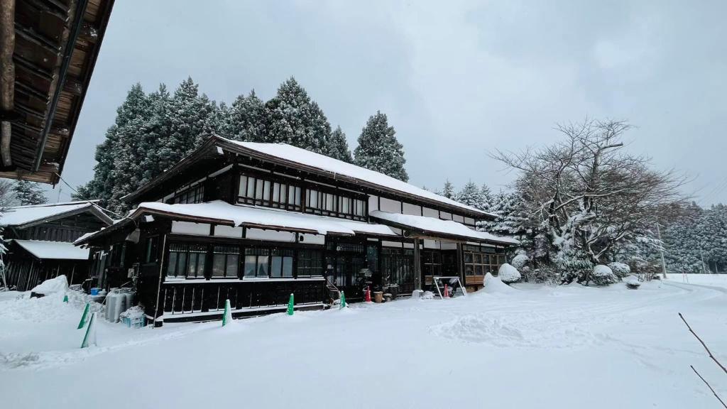 a building covered in snow with trees in the background at 農家民宿と古民家カフェ 里山のカフェ ににぎ in Oga