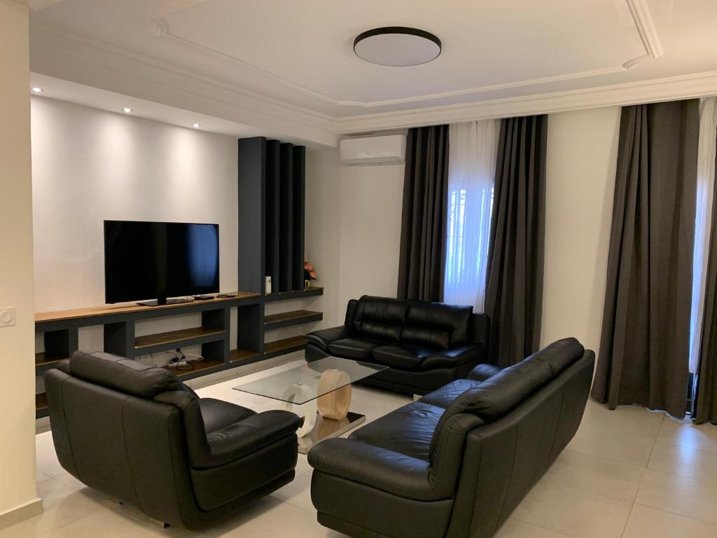 uma sala de estar com mobiliário de couro preto e uma televisão de ecrã plano em Superbe appartement spacieux em Iaundé