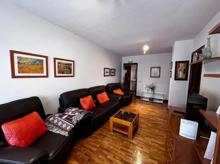 uma sala de estar com um sofá preto e almofadas laranja em Piso acogedor y luminoso cerca de hospitales em Pamplona
