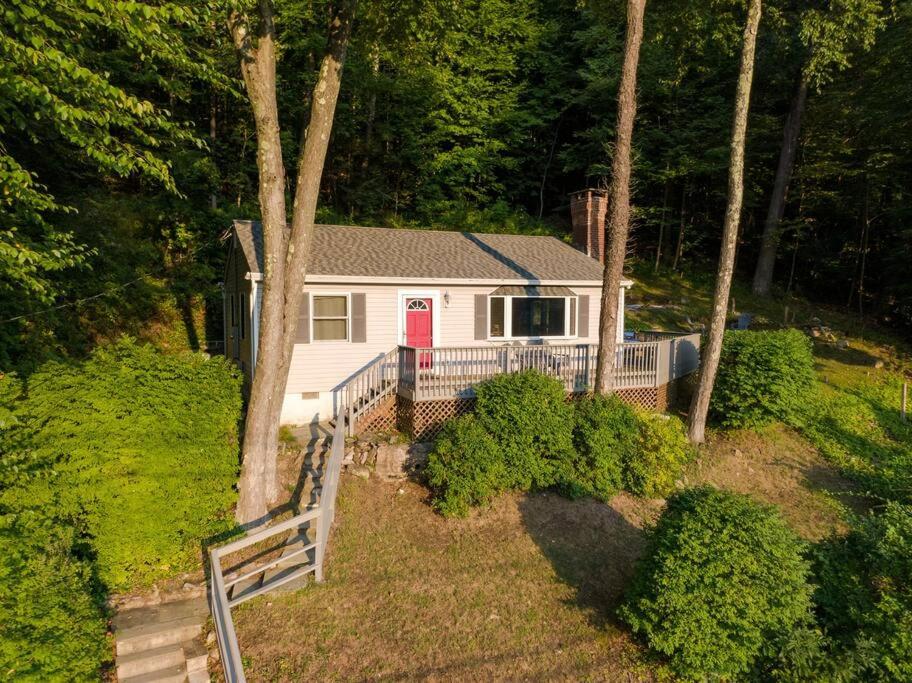 Ce cottage blanc dispose d'une porte rouge dans les bois. dans l'établissement Candlewood Lake Retreat with year round views, à New Milford