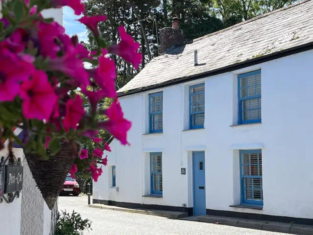 a white house with blue windows and pink flowers at Bell Cottage in Saint Teath